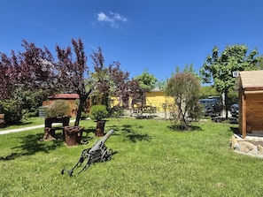 A grassy outdoor area with a wooden structure, a metal cannon, and various trees.