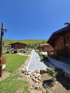 A pathway leading to wooden buildings with a clear sky and a forested hill in the background.