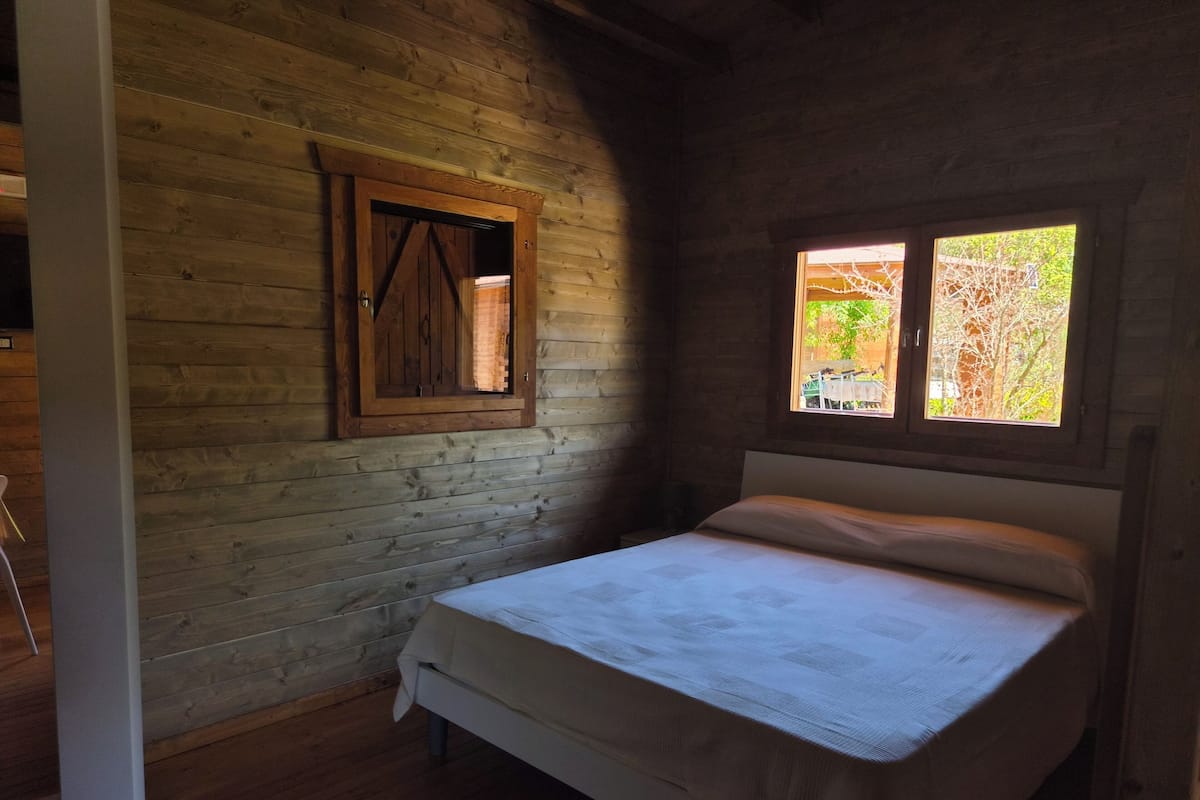 A wooden room with a bed, a window, and a wooden door.