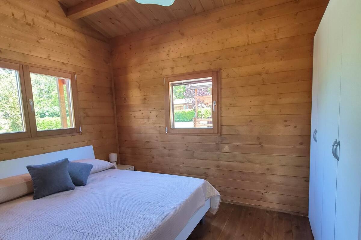 A wooden cabin bedroom with a bed, two windows, and a ceiling light.