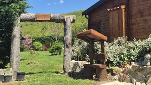 Une cabane rustique en bois, dotée d’une arche en bois sur laquelle est inscrit le mot « Gevnexulh », d’un banc en pierre et d’un mur de pierre orné de plantes en pot.