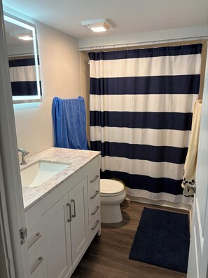 A bathroom with a white sink, a toilet, a striped shower curtain, and a blue towel on the wall. - Waterfront Resort Style Condo Near St Pete Beach (South Pasadena)