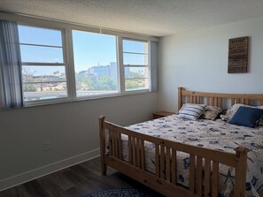 Ein Schlafzimmer mit einem hölzernen Bett, Blick auf die Stadt durch große Fenster und einem motivierenden Zitat an der Wand.