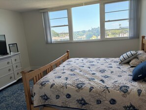 Ein Schlafzimmer mit Bett, Kommode und einem Fenster mit Blick auf Gebäude und Bäume.