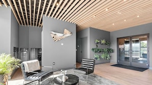 Un vestíbulo moderno con techo de listones de madera, una escultura de pez montada en la pared, un área de estar con sillas de cuero, una mesa redonda y un mostrador de recepción.