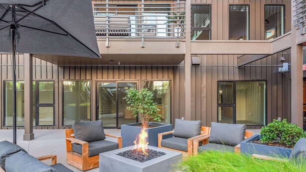 Un área de estar exterior moderna con fogones, mobiliario de madera y plantas en macetas.