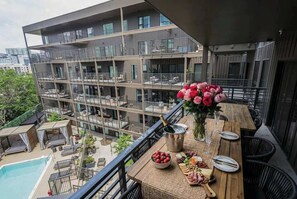 Ein Balkon mit Pool, einem Esstisch mit Speisen und Getränken und Blick auf ein mehrgeschossiges Gebäude.