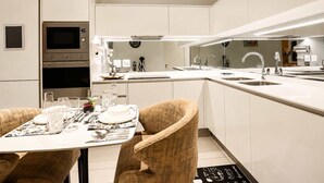 A modern kitchen with built-in appliances, a dining area with a table set for two, and a large island with a sink. - The Signature Luxury Stay (Midrand)