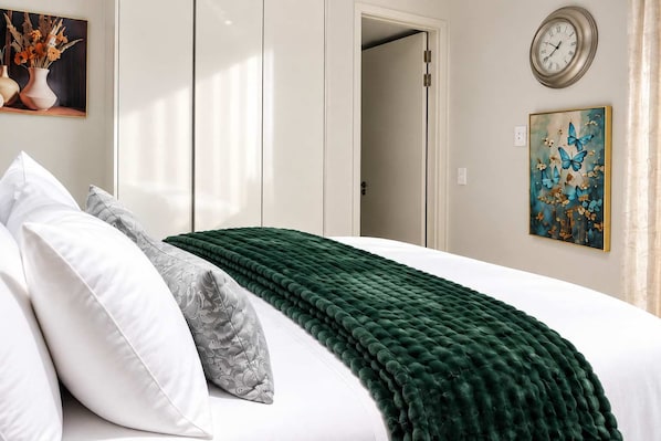 A neatly made bed with a green blanket, white pillows, and a grey patterned pillow.