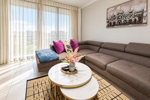 A modern living room with a sectional sofa, a round coffee table with a vase of flowers, and a painting on the wall.