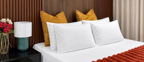 A neatly made bed with white bedding, a red throw blanket, and two mustard-colored pillows.