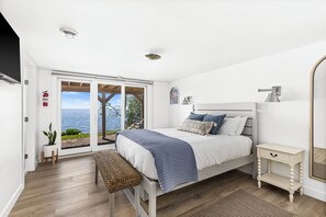 Ein Schlafzimmer mit einem Bett, einem Nachttisch, einer Bank, einem Feuerlöscher und Blick aufs Meer.