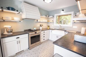 A kitchen with white cabinets, a stove, a sink, and a window.