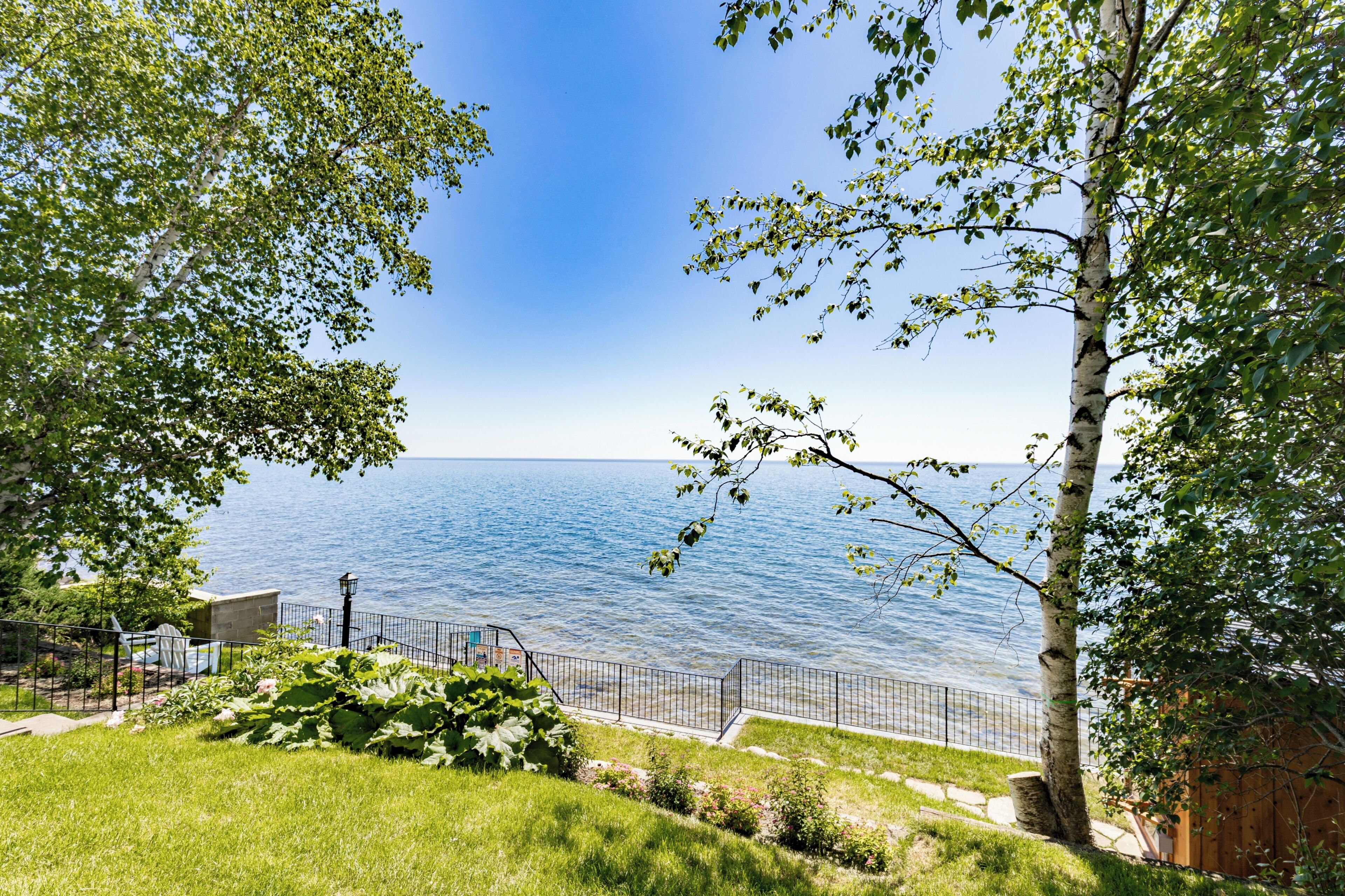 A coastal property with a view of the sea, a fenced pathway, and lush greenery.