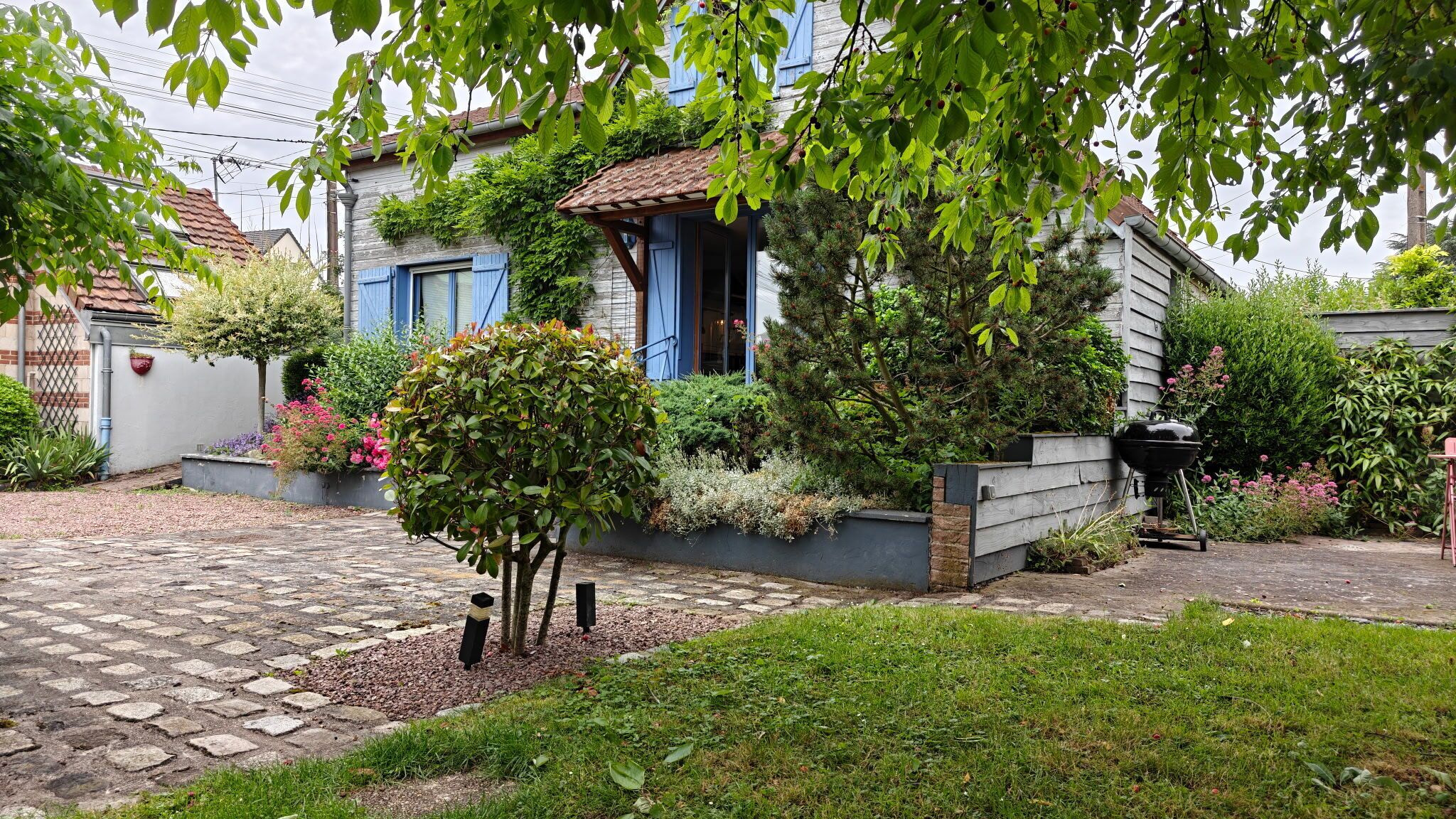 A residential property with a stone pathway, a small tree, and a garden with various plants.