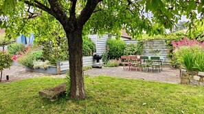 Un patio trasero con un árbol, una parrilla y mobiliario exterior.