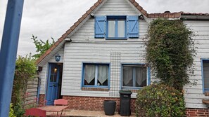 Una casa de dos pisos con cimientos de ladrillo, revestimiento blanco y contraventanas azules.