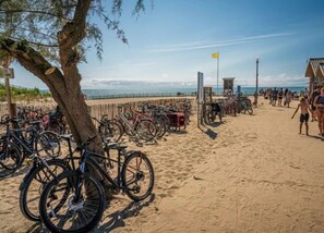 Une plage avec des vélos garés près d’un arbre et une tour de surveillance des sauveteurs en arrière-plan.