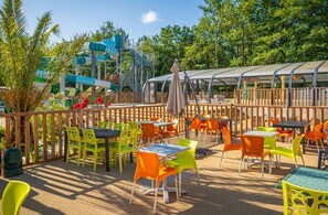 Une terrasse extérieure agrémentée de chaises et de tables colorées, d’un toboggan aquatique et d’un espace salon abrité.