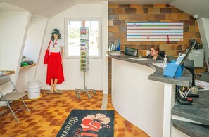 Un espace d’accueil comprenant un bureau, une chaise, un tableau d’affichage, une fenêtre et un sol carrelé.