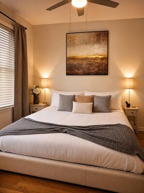 A bedroom with a bed, two bedside lamps, a ceiling fan, a painting, and a window with curtains. - King Bed Suite, 8 Min Airport, Fast WiFi & Gym (Jacksonville)