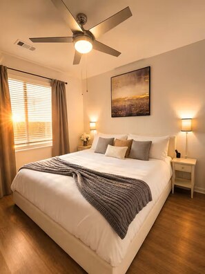 A bedroom with a bed, a ceiling fan, bedside lamps, a nightstand, and a painting on the wall. - King Bed Suite, 8 Min Airport, Fast WiFi & Gym (Jacksonville)