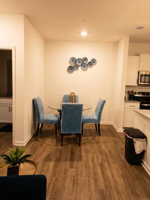 Un comedor con mesa de vidrio y sillas azules, una cocina con muebles blancos y piso de madera.