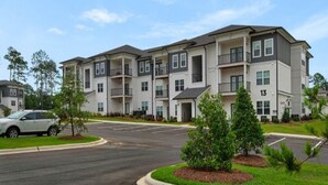 Een meerlaags appartementencomplex met balkons, een parkeerplaats en een heldere lucht.