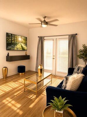 A modern living room with a flat-screen TV, a ceiling fan, a sofa, a coffee table, and a potted plant. - King Bed Suite, 8 Min Airport, Fast WiFi & Gym (Jacksonville)