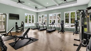 Een ruime fitnessruimte met loopbanden, krachtapparaten en plafondventilatoren.