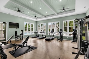 Ein großzügiger Fitnessraum mit Laufbändern, Kraftgeräten und Deckenventilatoren.