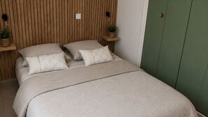 Een slaapkamer met een bed, kussens, een nachtkastje met een plant en een groene garderobe.