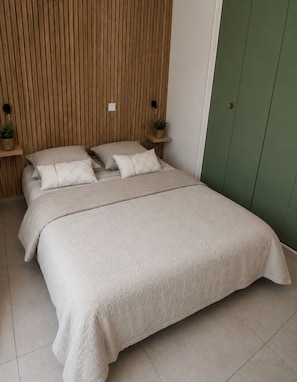 Ein Schlafzimmer mit einem Bett, Kissen, einem Nachttisch mit Pflanze und einem grünen Kleiderschrank.