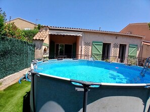 Ein Swimmingpool mit einer umlaufenden Sonnenterrasse, einer überdachten Veranda und einem Gebäude mit einem Ziegeldach und Fensterläden.