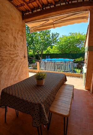 A covered patio with a table and bench, a pool in the background, and a view of trees. - Rosy House (Sanary-sur-Mer)