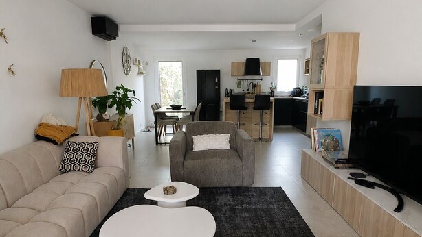 Een moderne woonkamer met een bank, twee witte salontafels, een televisie en een keuken op de achtergrond.