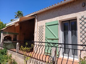 Ein Gebäude mit Balkon, einer Tür mit grünem Rollo und einem Fenster mit Gitterverzierung.
