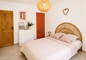A bedroom with a bed, a dresser, a wardrobe, a hanging light fixture, and a wall decoration. - Rosy House (Sanary-sur-Mer)