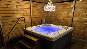 Un jacuzzi en una cabaña de madera con una escalera que lleva a él y una lámpara colgante arriba.
