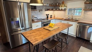 Una cocina moderna con una isla de madera, electrodomésticos de acero inoxidable, iluminación colgante y vistas al exterior.