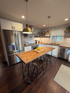A modern kitchen with a wooden island, stainless steel appliances, pendant lighting, and a view to the outside.