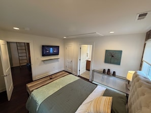 Un dormitorio con cama, televisor, obras de arte y vistas al pasillo.