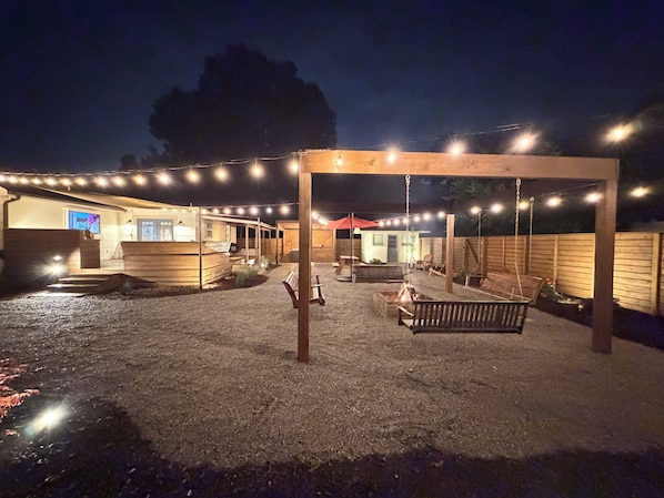 A covered outdoor area with string lights, wooden benches, and a fire pit.