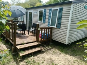 A mobile home with a deck, outdoor seating, and a covered patio area.
