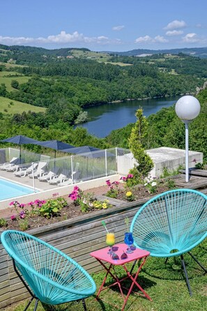 Une terrasse avec une piscine, des chaises et une vue sur un lac et des collines.
