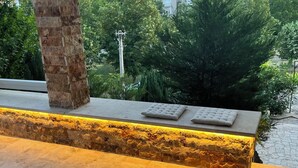 A stone bench with a cushion, a stone wall, and a view of buildings and trees in the background. - Riverside Luxury 3-bedroom apartment in beautiful Štip (Štip)