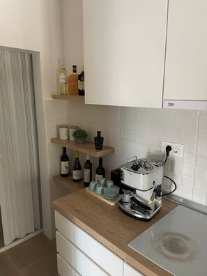 A kitchen with a wooden countertop, wine bottles, a coffee machine, and a dish rack.