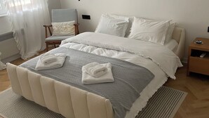 A neatly arranged bedroom with a bed, a chair, a nightstand, and three framed artworks on the wall. - Riverside Luxury 3-bedroom apartment in beautiful Štip (Štip)