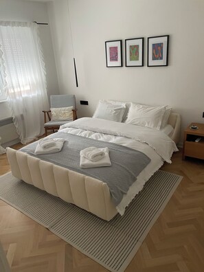 Ein ordentlich eingerichtetes Schlafzimmer mit einem Bett, einem Sessel, einem Nachttisch und drei gerahmten Kunstwerken an der Wand.