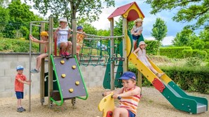 Kinder spielen auf einem Spielplatz mit Rutsche und Klettergerüsten.